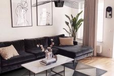 a chic living room with a black sectional, a geo printed rug, a white stone coffee table, a black chandelier and a gallery wall