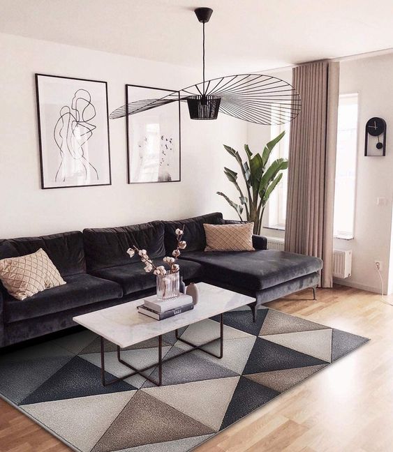 a chic living room with a black sectional, a geo printed rug, a white stone coffee table, a black chandelier and a gallery wall