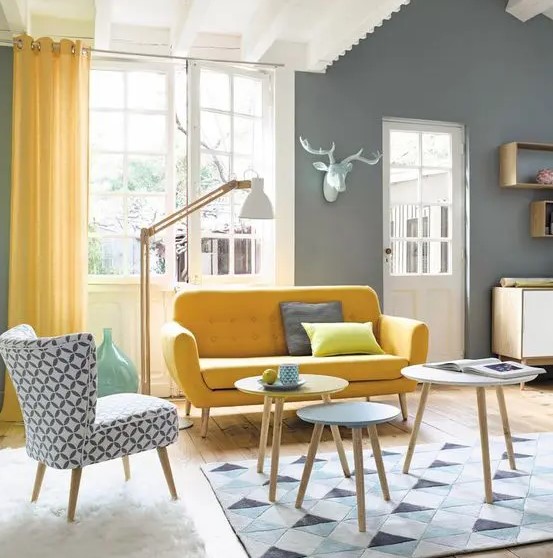 a chic living room with grey walls, a yellow sofa and a printed chair, yellow curtains, a geo printed rug and round coffee tables