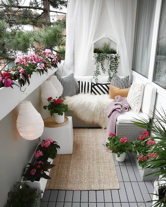 a chic yet small summer balcony in white, with sheer curtains, a jute rug, potted blooms, paper lanterns and printed textiles