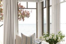 a coastal sunroom with a modern neutral daybed, striped pillows and neutral textiles plus gorgeous sea views