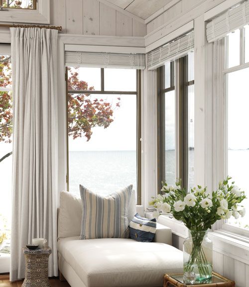 a coastal sunroom with a modern neutral daybed, striped pillows and neutral textiles plus gorgeous sea views