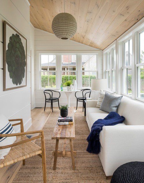 a coastal sunroom with mid century modern furniture, a navy blanket, a cool artwork and a woven pendant lamp