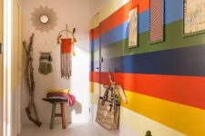 a colorful boho entryway with a rainbow accent wall, a bold rug, pendant lamps and hangings plus planters