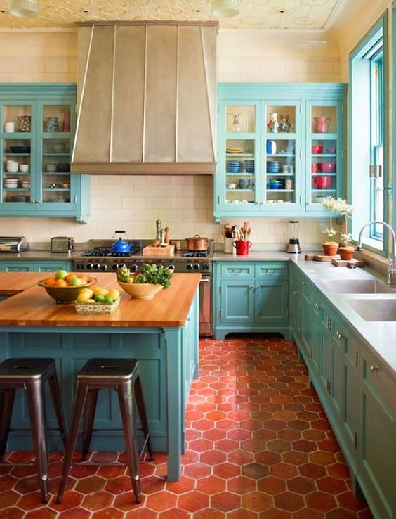 a colorful kitchen with turquoise kitchen with a large metal hood, a hexagon terracotta tile floor, a large kitchen island with a butcherblock countertop
