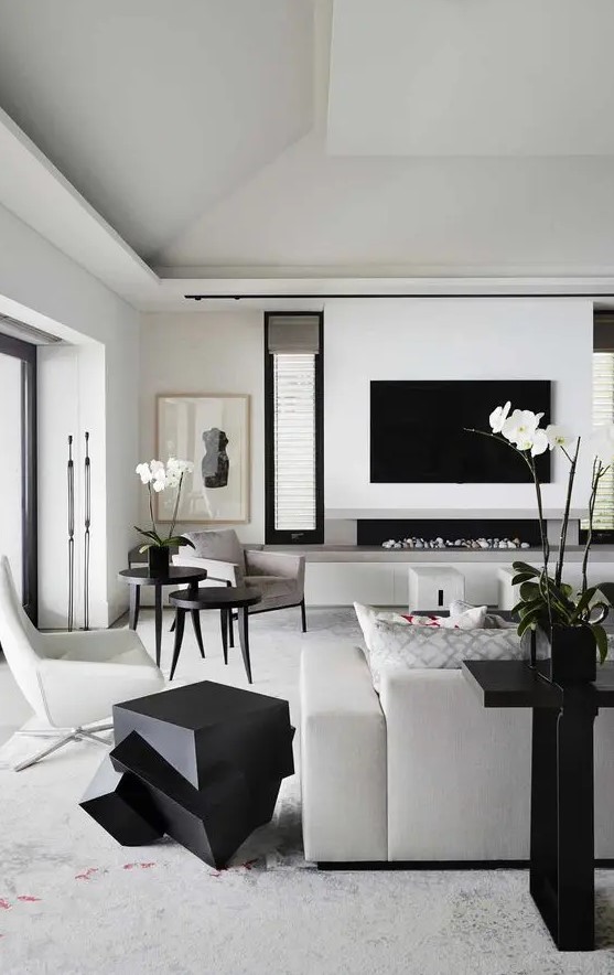 a contemporary black and white living room with a TV, a built-in fireplace, creamy and grey furniture, sculptural black tables and a console