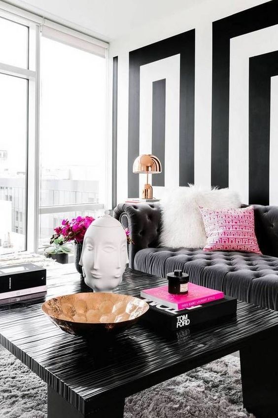 a contrasting living room with a black geo accent wall, a grey sofa with pink and white pillows, a black table, table lamps