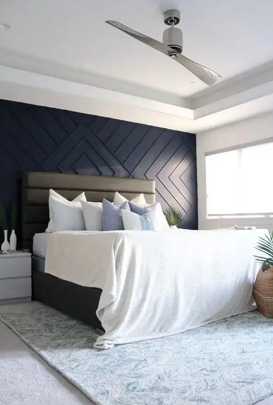 a cozy and airy bedroom with a navy geometric paneled wall, a leather upholstered bed, neutral nightstands, greenery in vases and pots