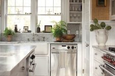 a cozy modern kitchen with white cabinets, grey stone cabinets, a grey marble backsplash, potted plants, a geo painted floor