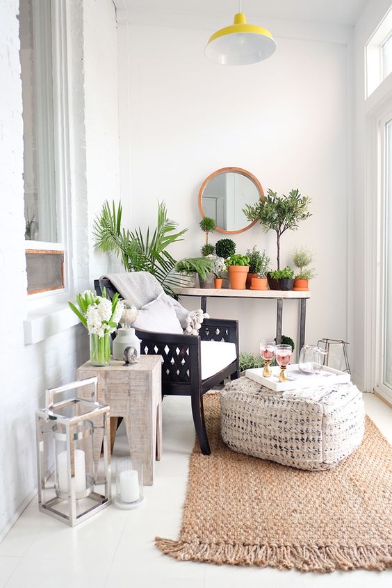 a cozy small sunroom with boho touches, a jute rug and ottoman, wooden chairs and lots of potted greenery and lanterns