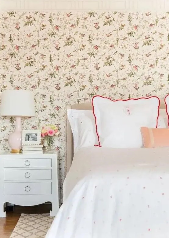 a cozy vintage inspired bedroom with a floral wallpaper wall, polka dot bedding, vintage inspired furniture and a blush lamp