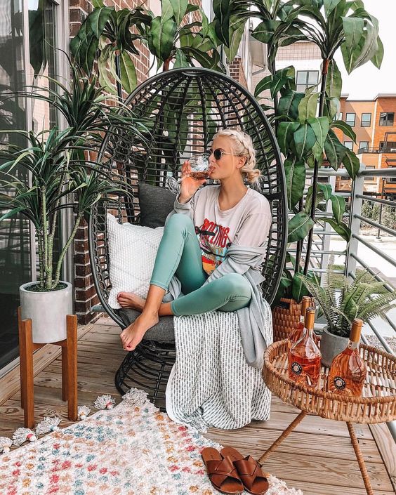 a cute small balcony with a large rattan egg chair and a rattan table, some statement plants and cozy textiles