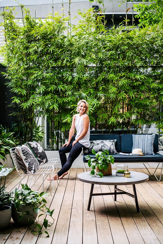 a fresh monochromatic terrace with a wooden deck, a greenery wall, greenery in pots and black and white furniture