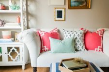 a fun and bright living room wiht white furniture, a pretty mini gallery wall, colorful pillows, a bright printed rug and a navy and white pouf