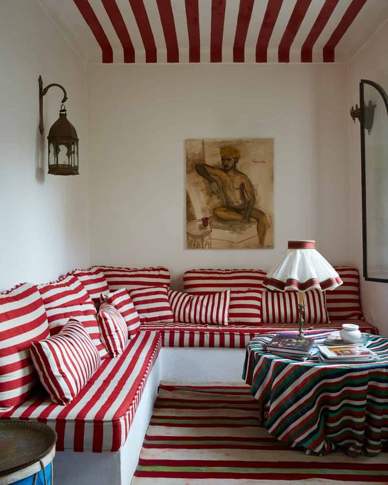 a gorgeous living room with a red and white striped ceiling, a matching corner bench with striped upholstery, a striped rug and a tablecloth