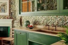 a green kitchen with butcherblock countertops, a bright floral wallpaper backsplash and glass cabinets is a stylish vintage-infused space