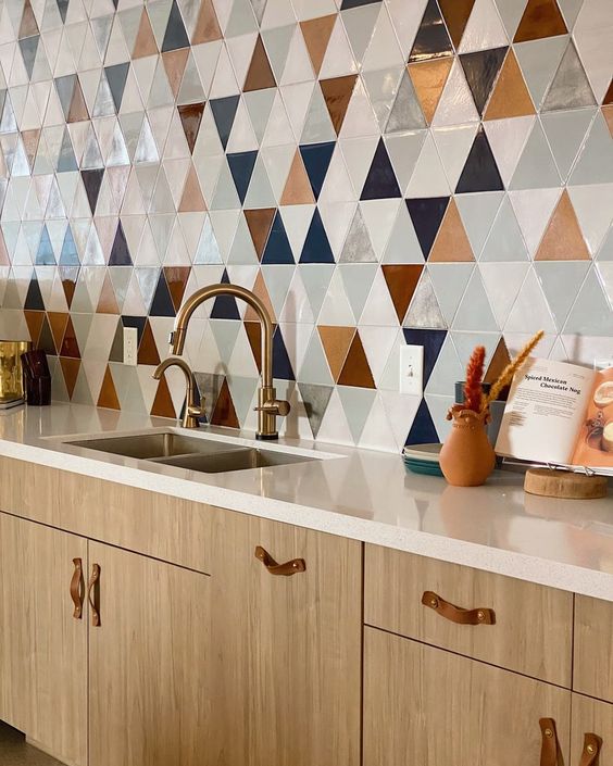 a light-stained kitchen with neutral stone countertops, a bold geo tile wall and leather handles and brass fixtures