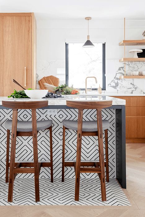a light-stained kitchen with white countertops and a marble backsplash, a chic kitchen island clad with black and white geo tiles