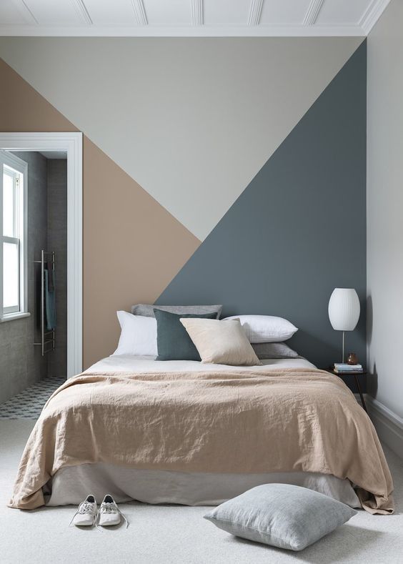 a lovely bedroom with a grey, rust and dark green geometric accent wall, a bed with matching in color bedding and a white lamp