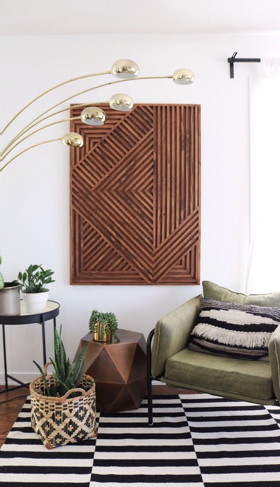 a lovely modern living room with a geometric stained artwork, a green chair with a boho pillow, a black and white striped rug, a faceted side table and a cool floor lamp