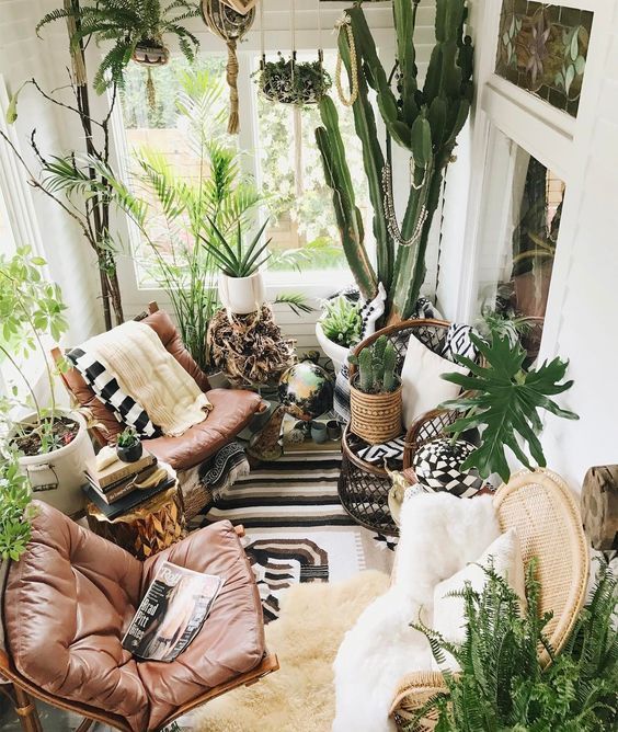 a lush boho sunroom with leather chairs, lots of potted greenery and some wicker and woven touches