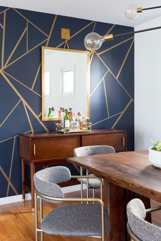 a mid-century modern dining room with a navy and gold geometric wall, a stained credenza and dining table, grey and brass chairs