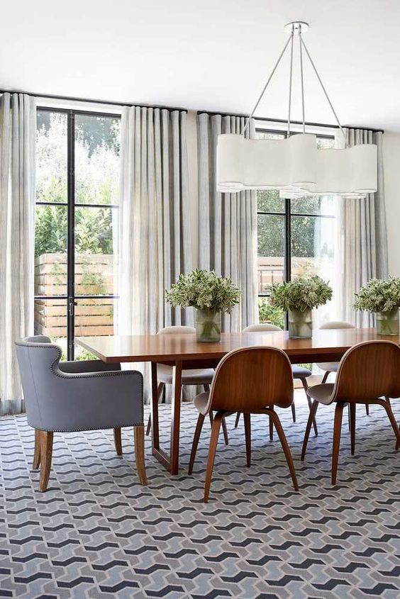 a mid-century modern dining room with a stained table and chairs, a grey chair with decorative nails, a stylish mid-century modern chandelier and a geo print rug