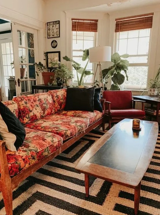 a mid century modern lviing room with a black and white rug, a floral sofa, rust colored chairs, potted plants and a floor lamp