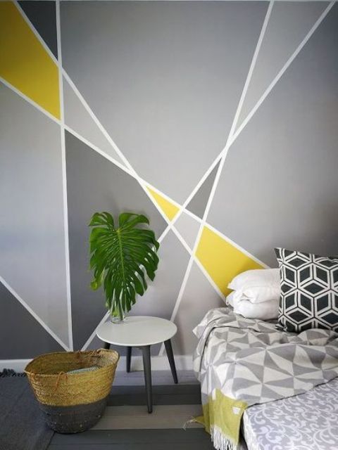 a modern bedroom with an accent grey and yellow accent wall, a bed with geometric bedding, a round nightstand, a leaf for decor