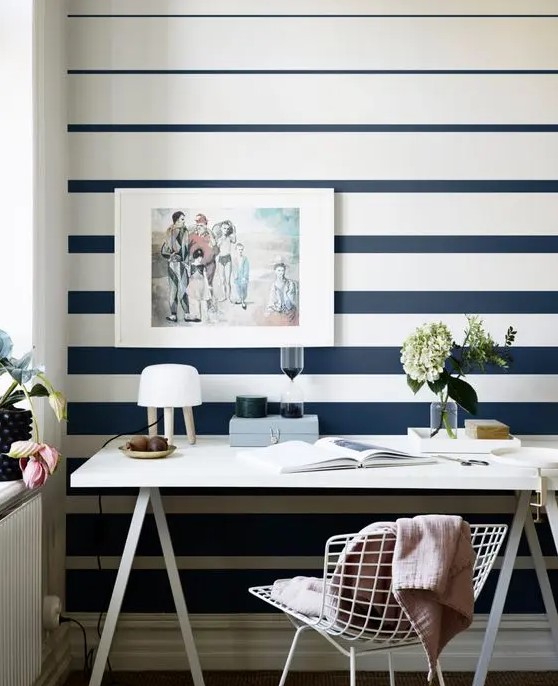 a modern home office with a striped navy and white striped wall, a trestle desk and a white metal chair