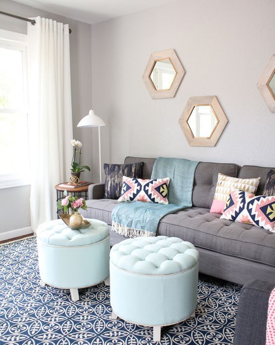 a modern living room with a grey sofa, aqua poufs, colorful pillows, hexagon-shaped mirrors in wooden frames