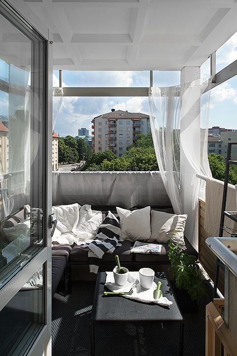 a monochromatic balcony with dark furniture, printed textiles, sheer curtains and potted greenery