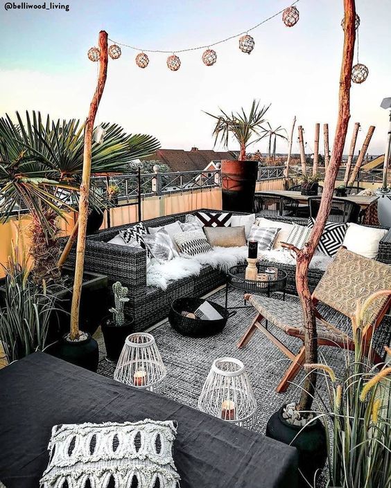 a monochromatic summer terrace with black furniture, black and white textiles, candle lanterns and potted greenery and trees