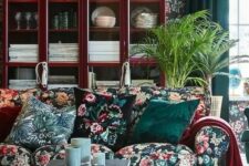 a moody living room with dark floral wallpaper and a matching sofa, floral pillows, a rich-stained buffet, a couple of coffee tables