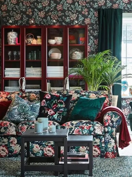 a moody living room with dark floral wallpaper and a matching sofa, floral pillows, a rich stained buffet, a couple of coffee tables