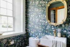 a moody powder room with dark green floral wallpaper, a stained vanity, a mirror in a chic frame and white appliances