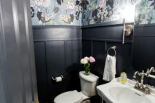 a moody powder room with grey floral wallpaper and black panling, a free-standing sink and a toilet, some blooms