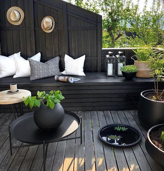 a moody terrace with black wood, light pillows, potted greenery and candle lanterns looks fresh and stylish