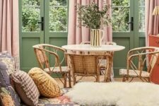 a muted color living room with green walls and doors, pink curtains, a floral daybed and a rattan dining nook