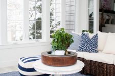 a nautical sunroom with a dark rattan sectional, striped poufs, a vintage table and a potted plant