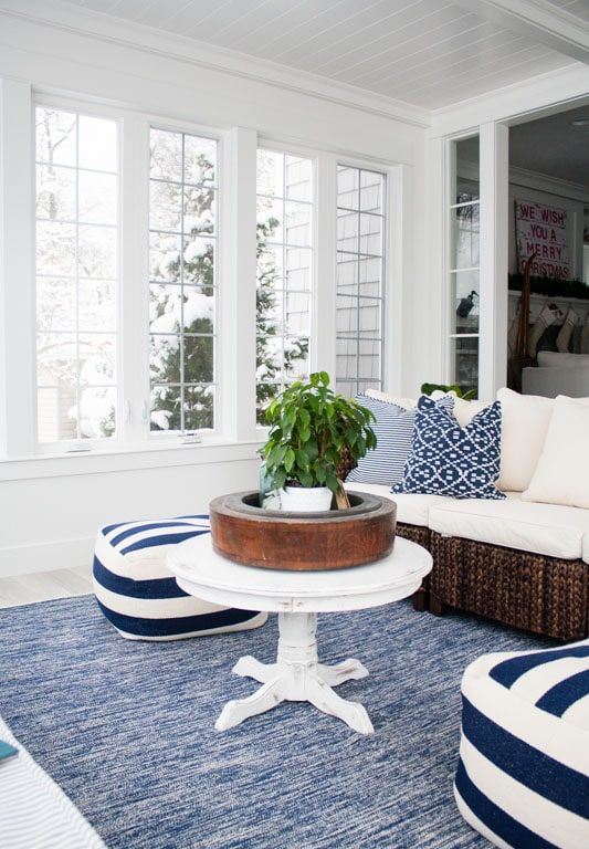 a nautical sunroom with a dark rattan sectional, striped poufs, a vintage table and a potted plant