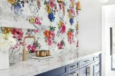 a navy and white kitchen with shaker cabinets, white marble countertops, a bright floral wallpaper wall and open shelves plus brass touches