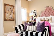 a refined and chic bedroom with tan walls, a pink bed with an extended headboard, a striped sofa and a pink pouf, a zebra printed rug