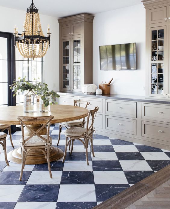 a refined vintage dining room with a black and white checked floor, a wooden dining set, taupe shaker style cabinetry