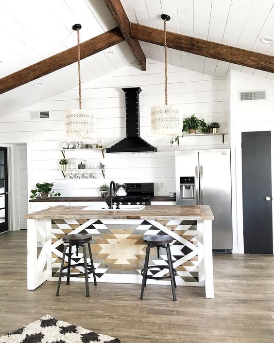 a rustic boho kitchen with shiplap walls and a ceiling, white cabinets with a dark-stained countertop, a kitchen island with geo decor, dark stools and boho pendant lamps
