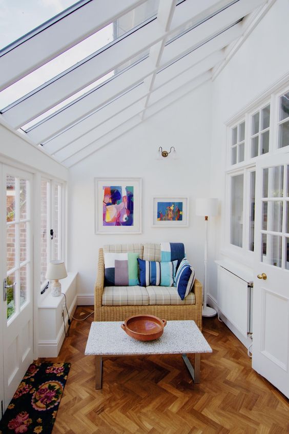 a simple and modern sunroom with a small wicker sofa with colorful pillows, artworks and a coffee table