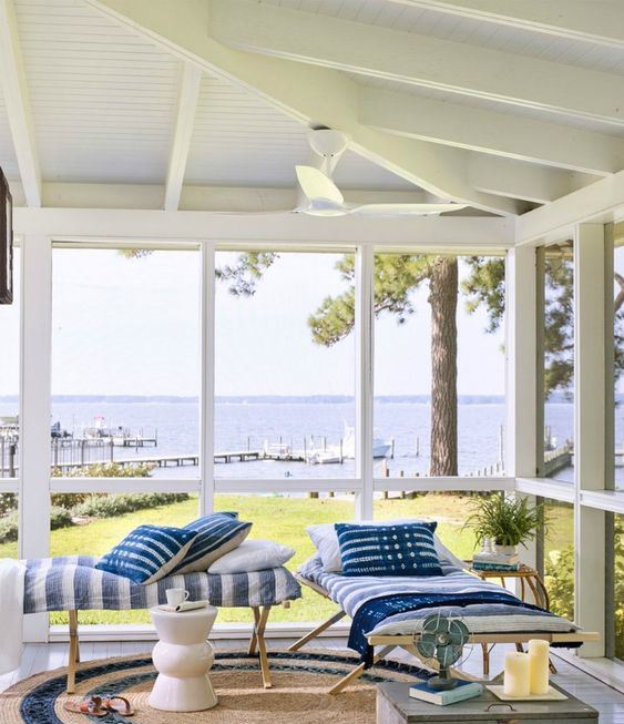 a simple beach sunroom with wooden daybeds, printed textiles, a wooden chest and candles plus cool views