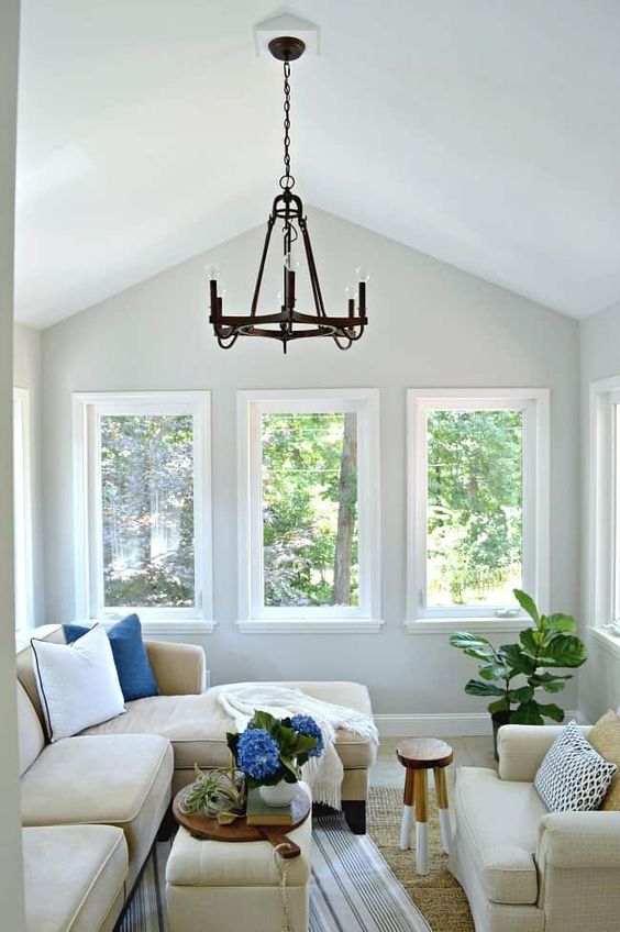 a small and cozy sunroom with neutral furniture, a couple of ottomans and some greenery feels like an additional living room