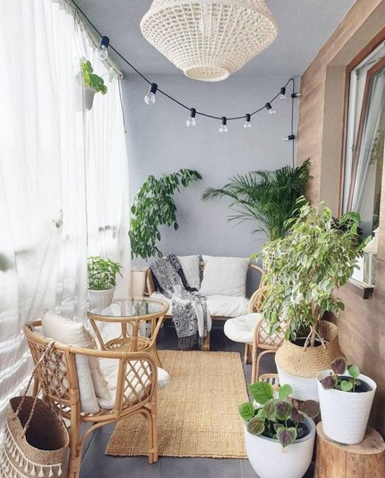 a small balcony with sheer curtains, lights, a wicker lamp, rattan furniture, statement plants and baskets is very cozy