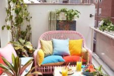 a small bright balcony with a pink loveseat, a small table, a white bench with storage, potted greenery and bright pillows